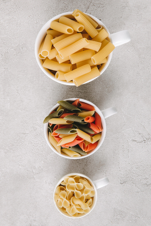top view of various types of raw pasta in bowls standing in row on concrete tabletopの写真素材
