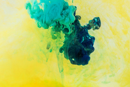 background with green and turquoise paint flowing in yellow waterの写真素材
