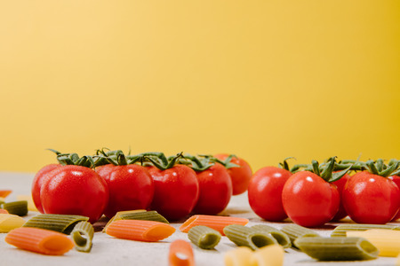 close-up shot of cherry tomatoes and raw colored pasta on yellowの写真素材