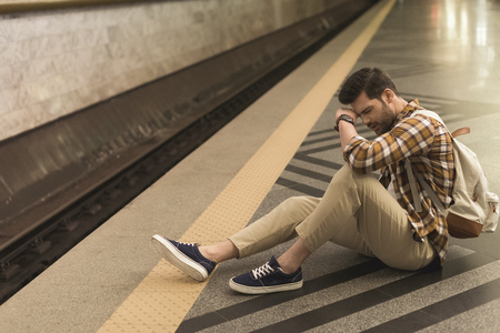 upset young man with backpack late on train and sitting on floor at subway stationの写真素材