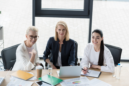 high angle view of beautiful businesswomen looking at camera at meeting in officeの写真素材