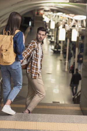 couple of stylish tourists with backpacks holding hands and going at subway stationの写真素材