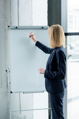 side view of professional businesswoman writing on blank whiteboard in officeの写真素材