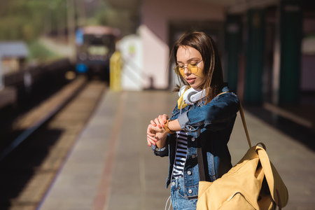 stylish woman in sunglasses with headphones and backpack looking at wristwatchの写真素材