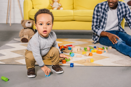 adorable african american toddler looking at camera while playing with father at homeの写真素材