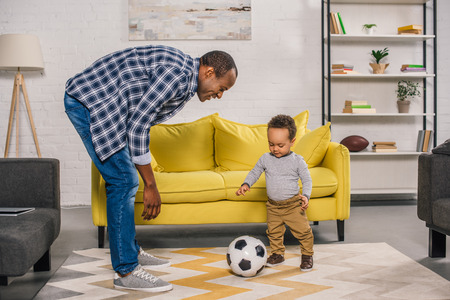 happy young father looking at smiling little son playing with soccer ball at homeの写真素材