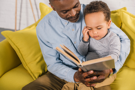cropped shot of grandfather and grandson reading book at homeの写真素材