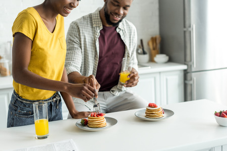 cropped image of african american couple eating pancakes and drinking orange juice at kitchenの写真素材