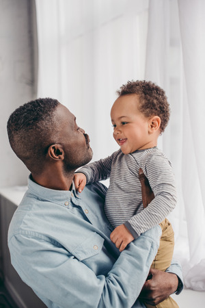 happy african american grandfather and grandchild smiling each other at homeの写真素材