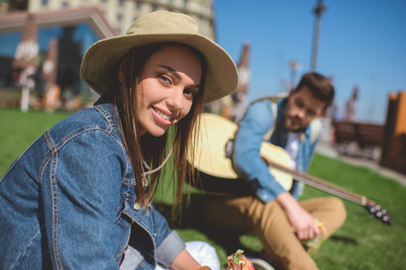 attractive smiling woman in hat and boyfriend sitting behind with guitarの写真素材