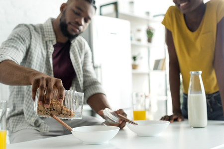 cropped image of african american boyfriend pouring out cornflakes into plate at kitchenの写真素材
