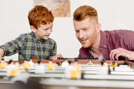 happy redhead father and son playing table football together at home
