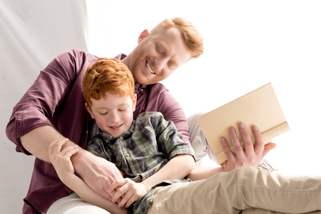 happy father and son having fun together while reading book at homeの写真素材