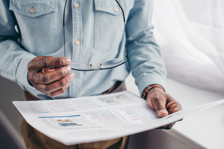 cropped shot of senior african american man holding eyeglasses and reading newspaperの写真素材