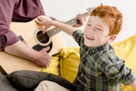 cropped shot of cute little boy laughing and father playing guitarの写真素材