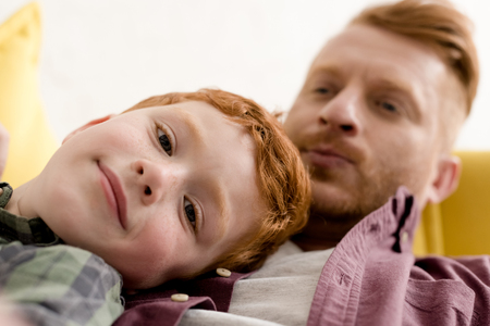 close-up view of cute little boy smiling at camera while spending time with father at homeの写真素材