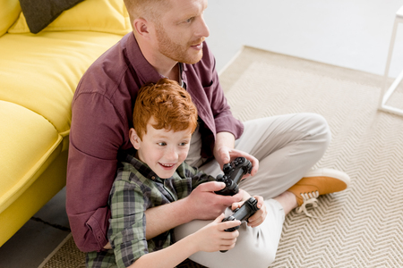 high angle view of happy father and son playing with joysticks at home