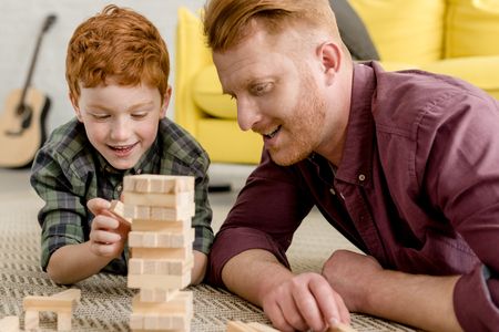 happy redhead father and son lying on carpet and playing with wooden blocksの写真素材