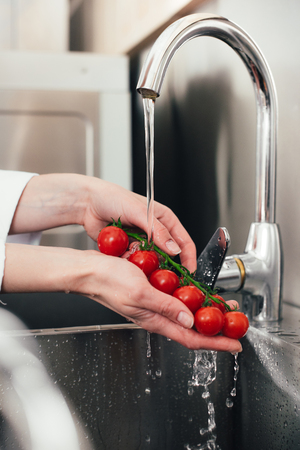 Close-up view view of female chef washing tomatoesの写真素材