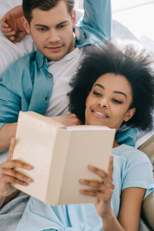 Relaxed couple reading book while lying in bedの写真素材