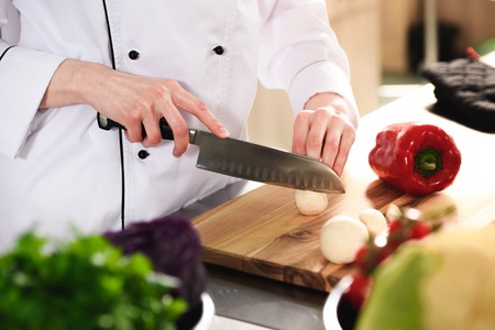 Close-up view of female chef cutting mushrooms on wooden board