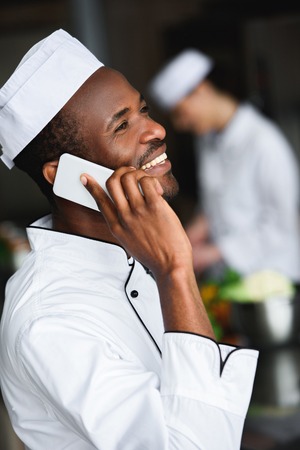 side view of smiling african american chef talking by smartphone at restaurant kitchenの写真素材