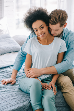 Young tender multiracial couple hugging on bedの写真素材
