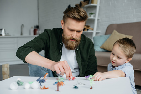 father and cute little son playing with various toy dinosaurs together at homeの写真素材