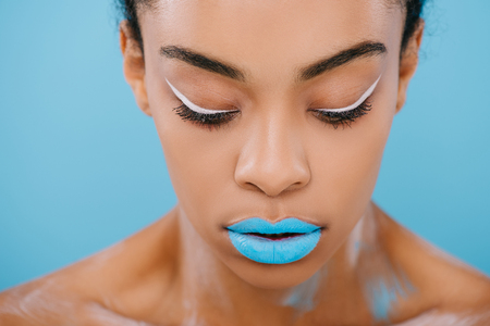 close-up portrait of african american woman with creative makeup and perfect skin isolated on blueの写真素材