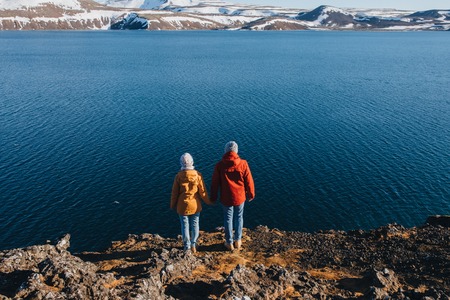 back view of couple standing on rocky coast and looking at majestic icelandic landscapeの写真素材