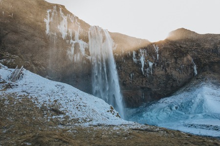 beautiful icelandic landscape with Seljalandsfoss waterfall, snow on rocks and sunshine
