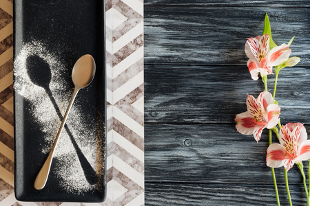 top view of spoon with powder ready for dessert and beautiful flowers on wooden table