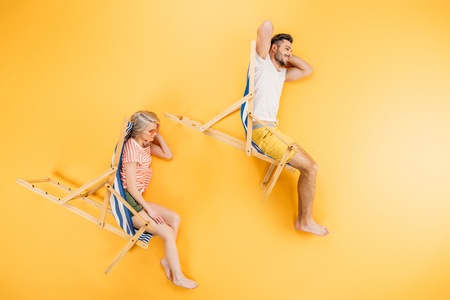 happy young couple resting in beach chairs on yellow, summer vacation conceptの写真素材