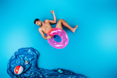 young man holding swimming ring and looking at imagine sea with beach ball and toy ships on blueの写真素材