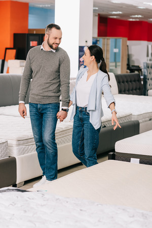 couple holding hands while choosing mattress together in furniture storeの写真素材