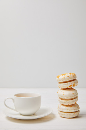 closeup shot of coffee cup and stack of macarons on white wooden tableの写真素材
