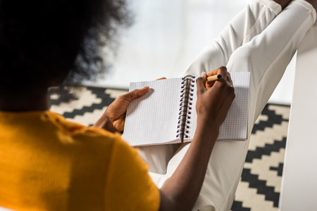 partial view of african american freelancer making notes in notebook at home officeの写真素材