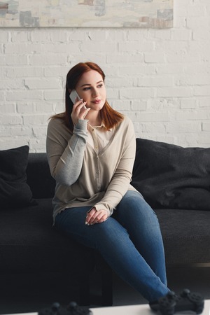 beautiful girl talking by smartphone on sofa at homeの写真素材