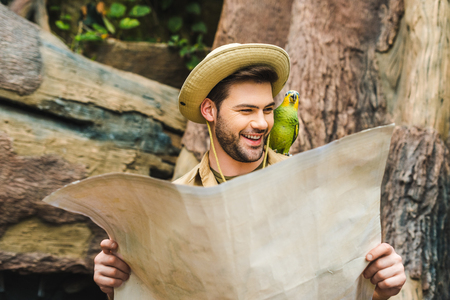 happy young man with parrot on shoulder and map in jungleの写真素材
