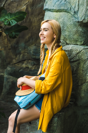 smiling young woman in straw hat relaxing on rocks outdoorsの写真素材