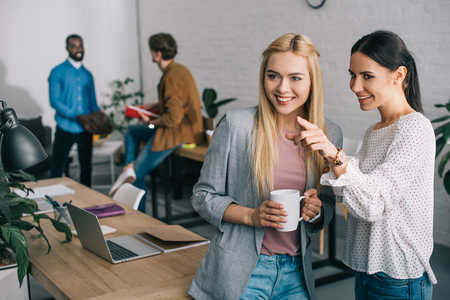 smiling businesswoman pointing by finger to colleague and two coworkers standing behind in modern officeの写真素材