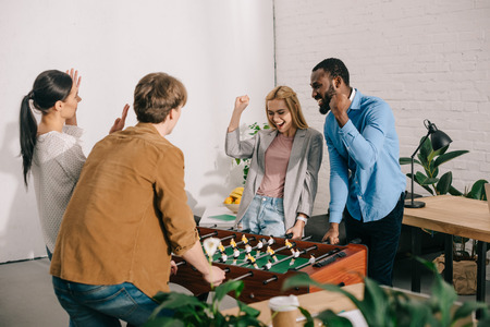 happy multicultural business colleagues gesturing and playing table football in modern office