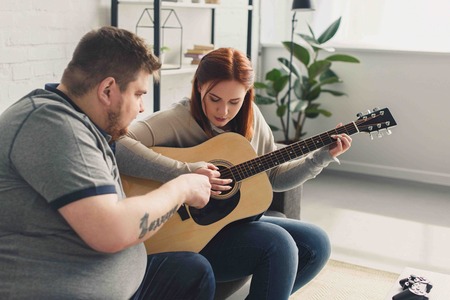 boyfriend teaching girlfriend playing acoustic guitar at homeの写真素材