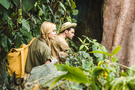 active young couple in safari suits hiking in jungle and looking somewhere impressedの写真素材