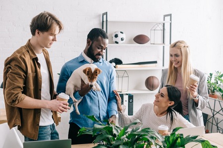 african american businessman holding jack russell terrier and smiling colleagues standing nearの写真素材