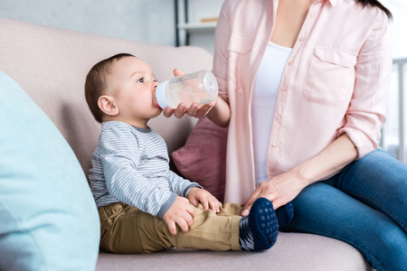 cropped shot of mother feeding her little child with bottle at homeの写真素材