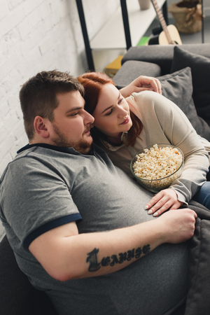 boyfriend and girlfriend hugging on sofa with popcorn and watching tv at homeの写真素材