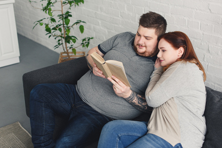 boyfriend and girlfriend reading book together on sofa in living roomの写真素材
