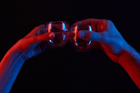 cropped shot of man and woman clinking glasses under toned light isolated on blackの写真素材