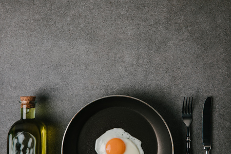 top view of frying pan with fried egg, cutlery and bottle of oil on greyの写真素材